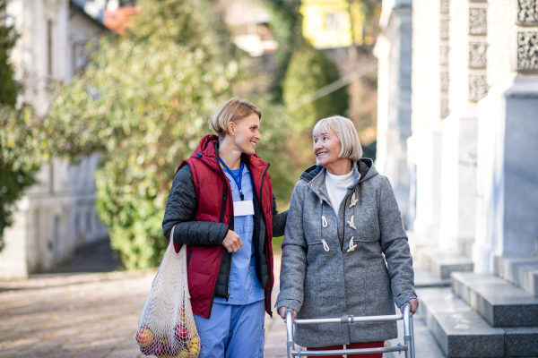 Happy senior woman with walking frame and caregiver outdoors in town, shopping and coronavirus concept.