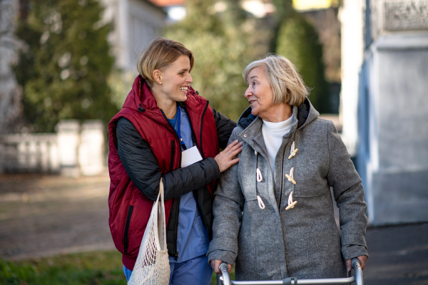 Happy senior woman with walking frame and caregiver outdoors in town, shopping and coronavirus concept.