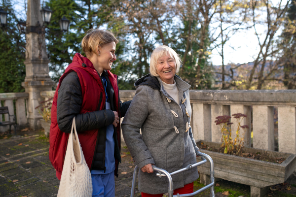 Happy senior woman with walking frame and caregiver outdoors in town, shopping and coronavirus concept.