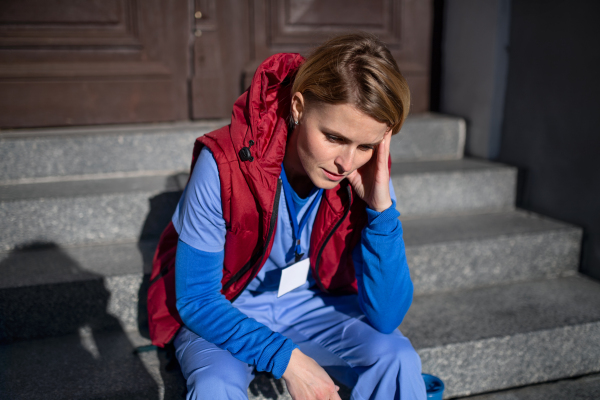 Tired woman caregiver, nurse or healthcare worker sitting outdoors on front steps on the way to work.