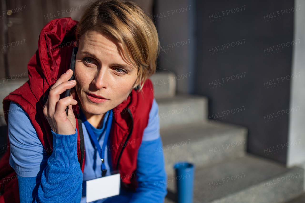 Tired woman caregiver or healthcare worker with smartphone having a break outdoors, coronavirus concept.