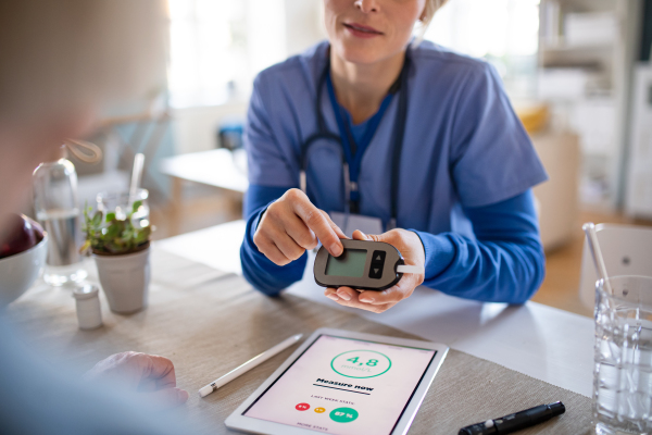 Nurse, caregiver or healthcare worker with senior woman patient, measuring blood glucose indoors.