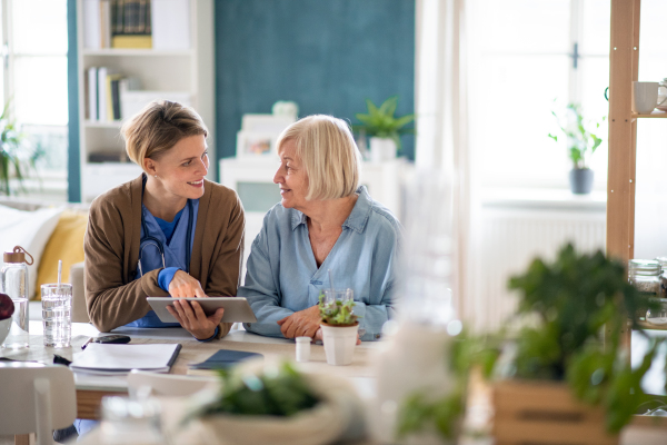 Caregiver or healthcare worker with senior woman patient, using a tablet and explaining.