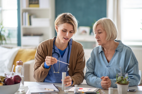 Caregiver or healthcare worker with senior woman patient, explaining how to use litmus paper strip.