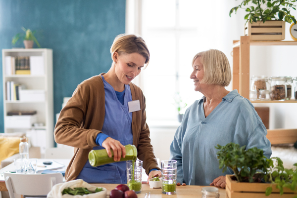 Senior woman with caregiver or healthcare worker indoors, drinking healthy smoothie drink.