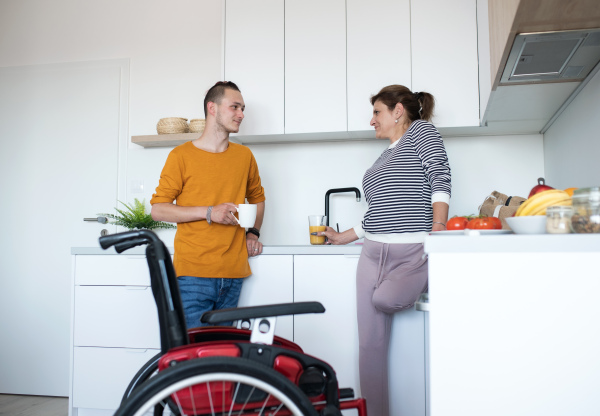 Disabled mature woman with leg amputee talking to her son in kitchen indoors at home.