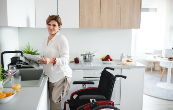 A portrait of disabled mature woman in wheelchair indoors at home, preparing breakfast.