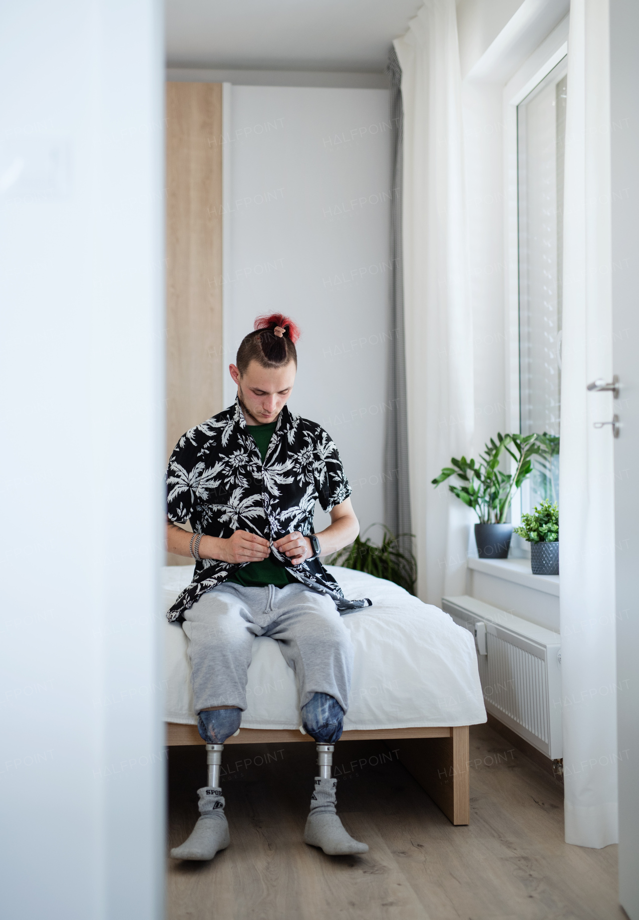 Front view portrait of disabled young man sitting in bed indoors at home, leg prosthetic concept.