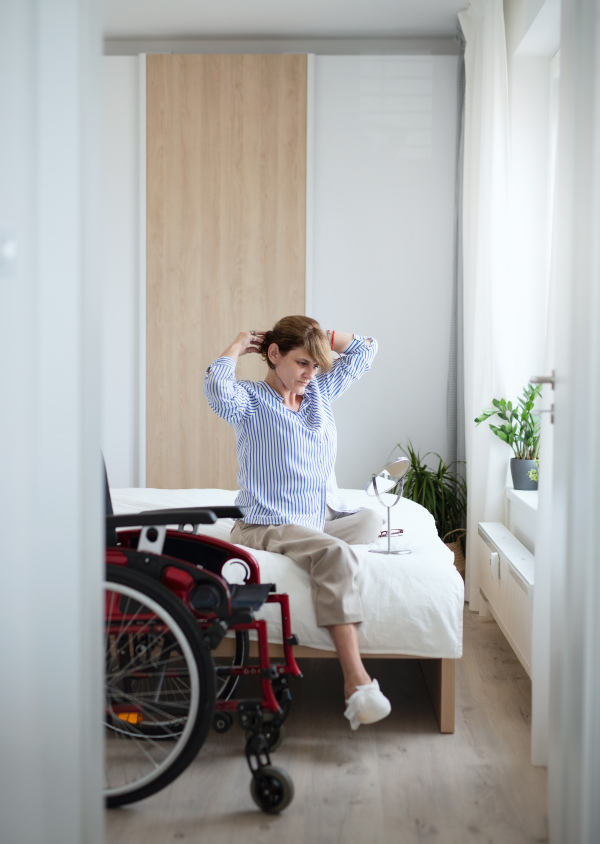 Portrait of disabled mature woman sitting on bed indoors at home, morning routine with leg amputee concept.