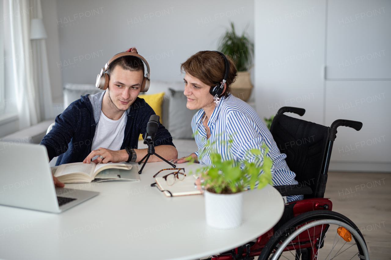 Happy disabled people sitting at the table indoors at home, recording podcast at home.