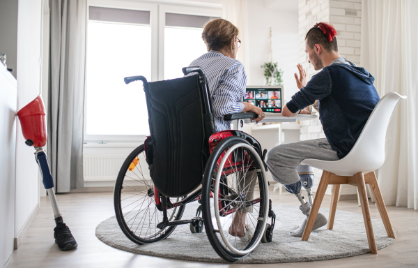 A rear view of disabled people sitting at the table indoors at home, video call concept.