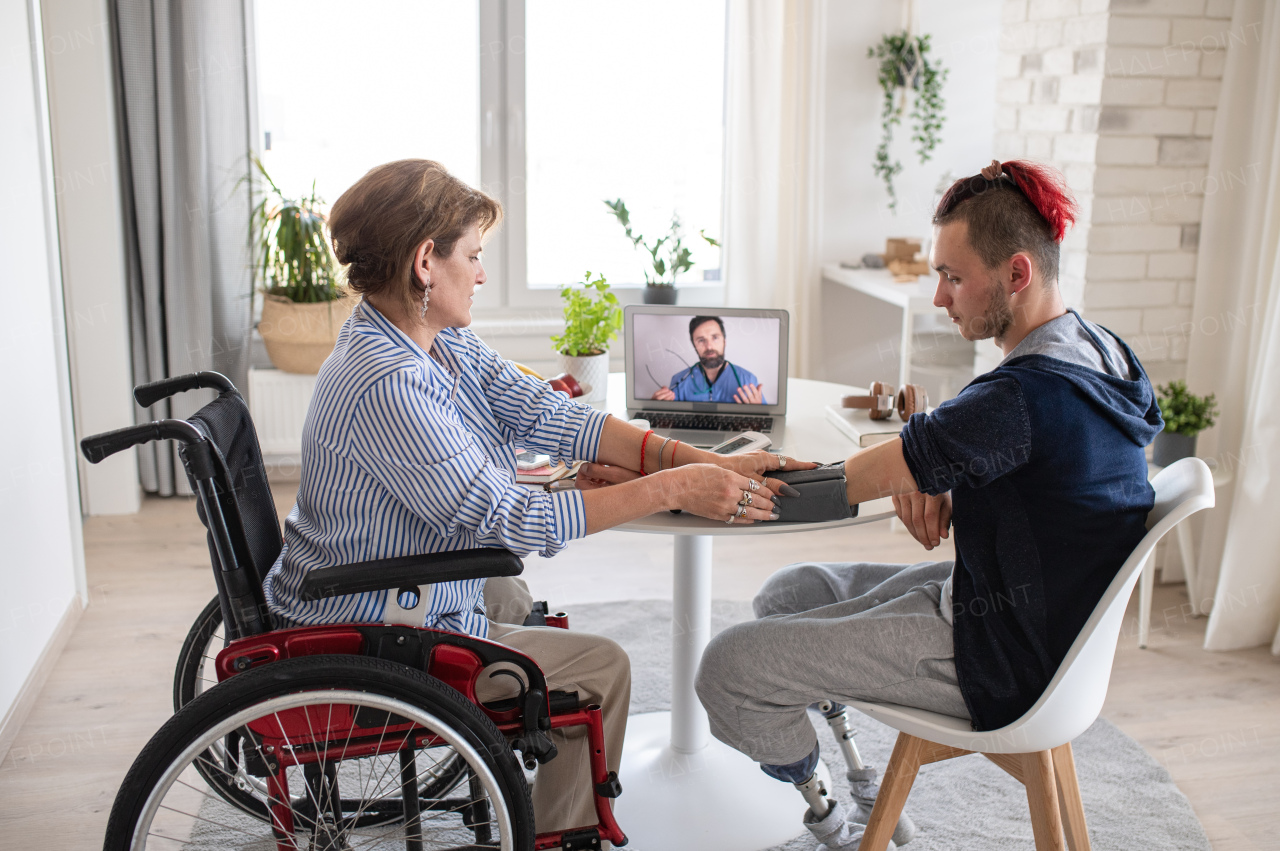 Disabled people sitting at the table indoors at home, video online consultation with doctor.