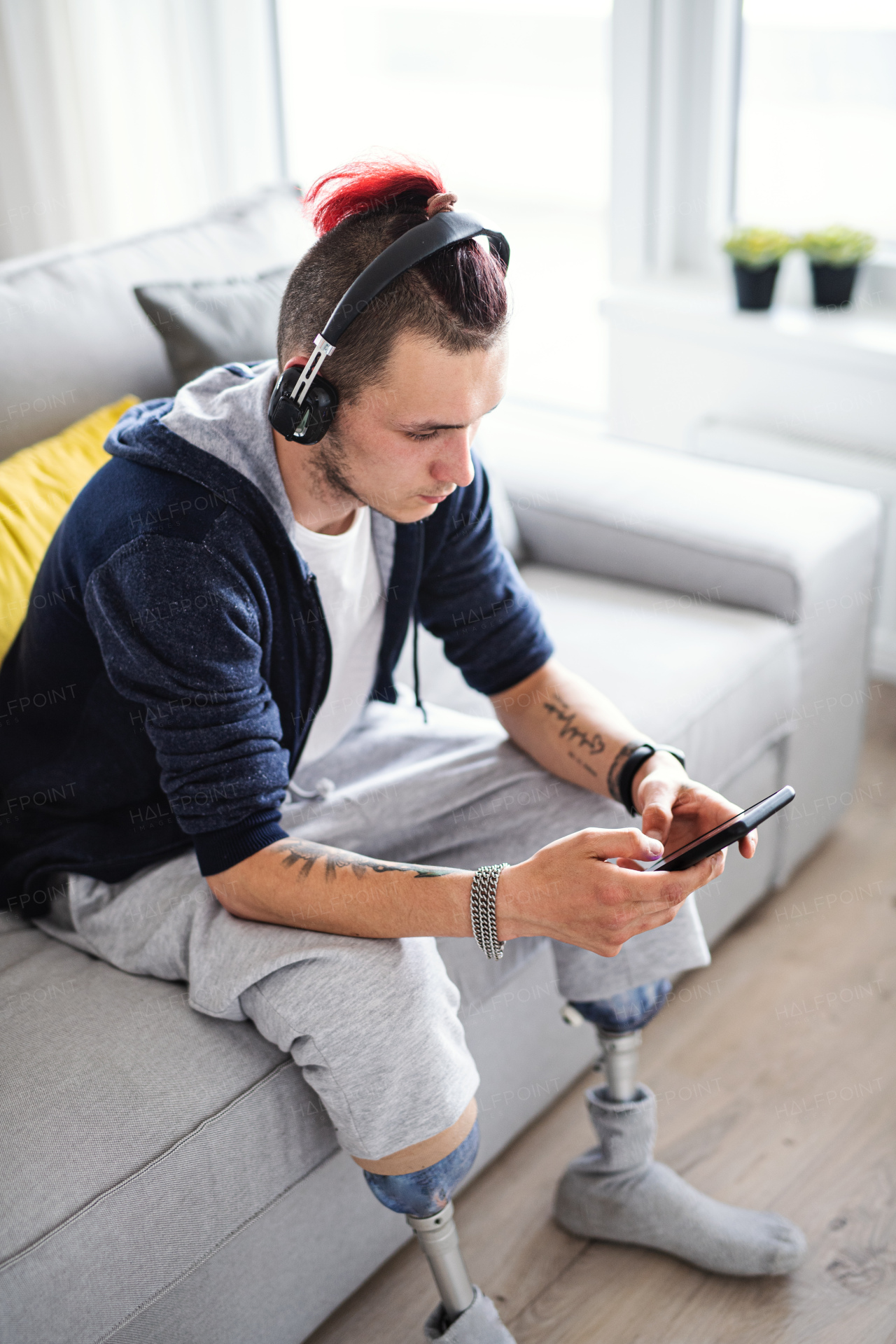 A portrait of disabled young man using smartphone indoors at home, leg prosthetic concept.