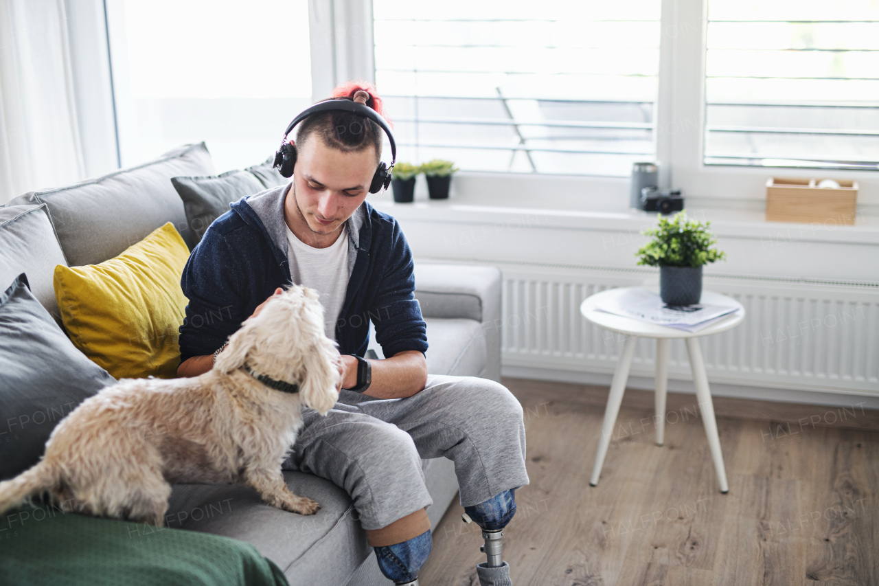 A portrait of disabled young man playing with dog indoors at home, leg prosthetic concept.