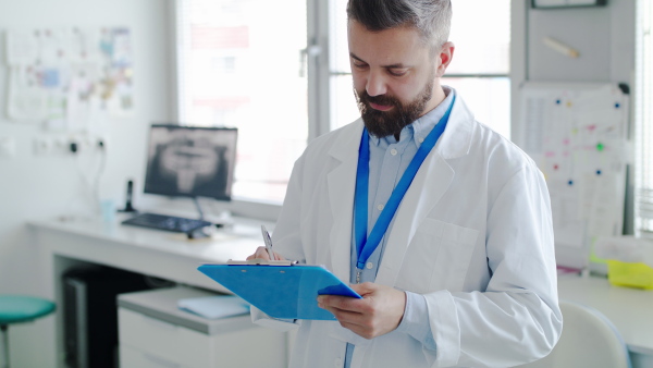 A mature dentist with clipboard in modern dental surgery, working.