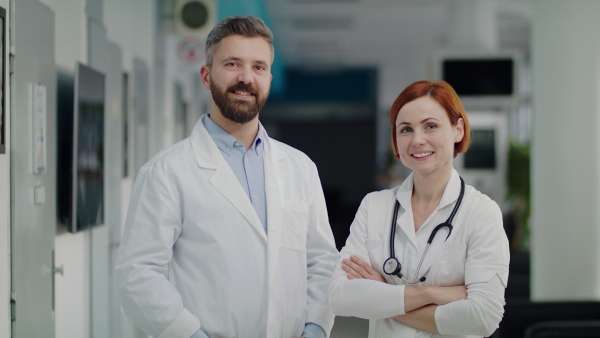 A portrait of man and woman doctor standing in hospital, looking at camera.