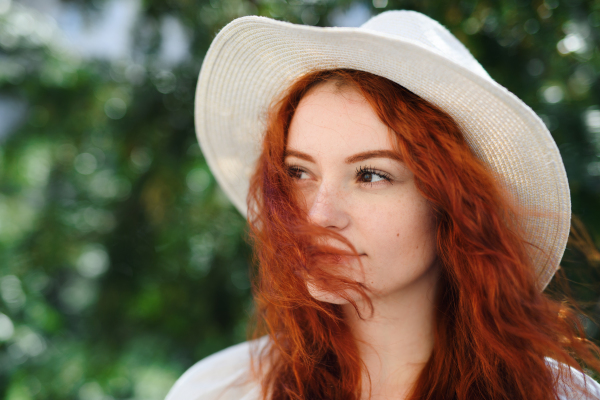 A close-up portrait of young woman with hat outdoors in city, headshot.