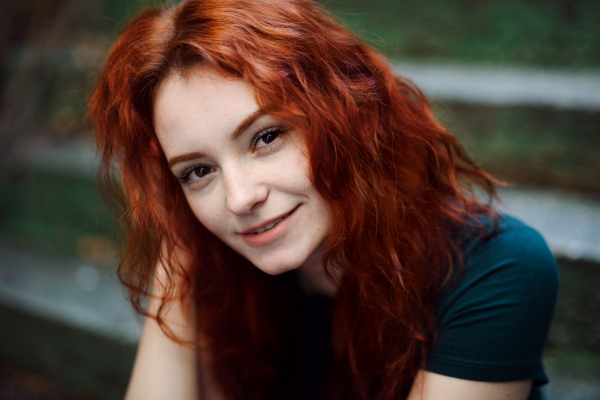 A portrait of young woman sitting outdoors on staircase in city, looking at camera.