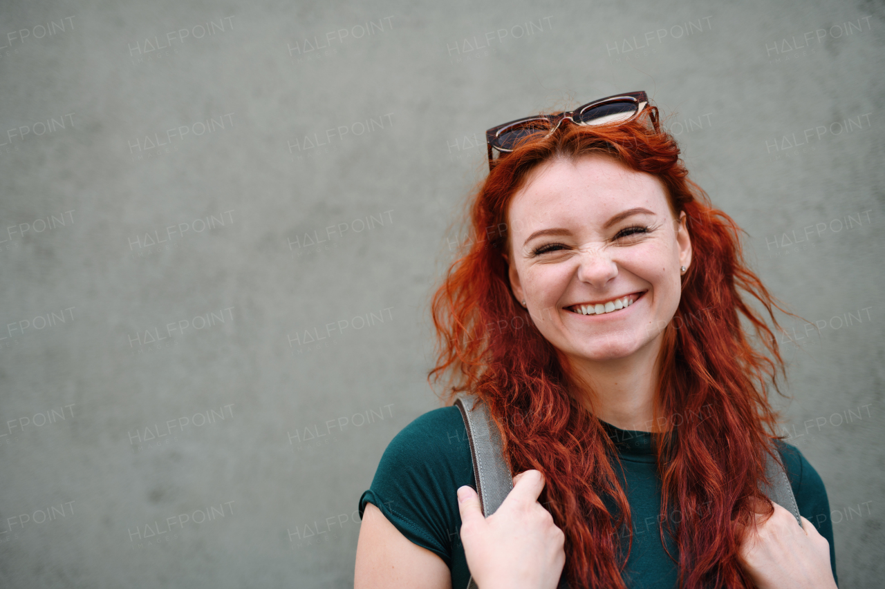 A portrait of young laughing woman standing outdoors against gray background, looking at camera.