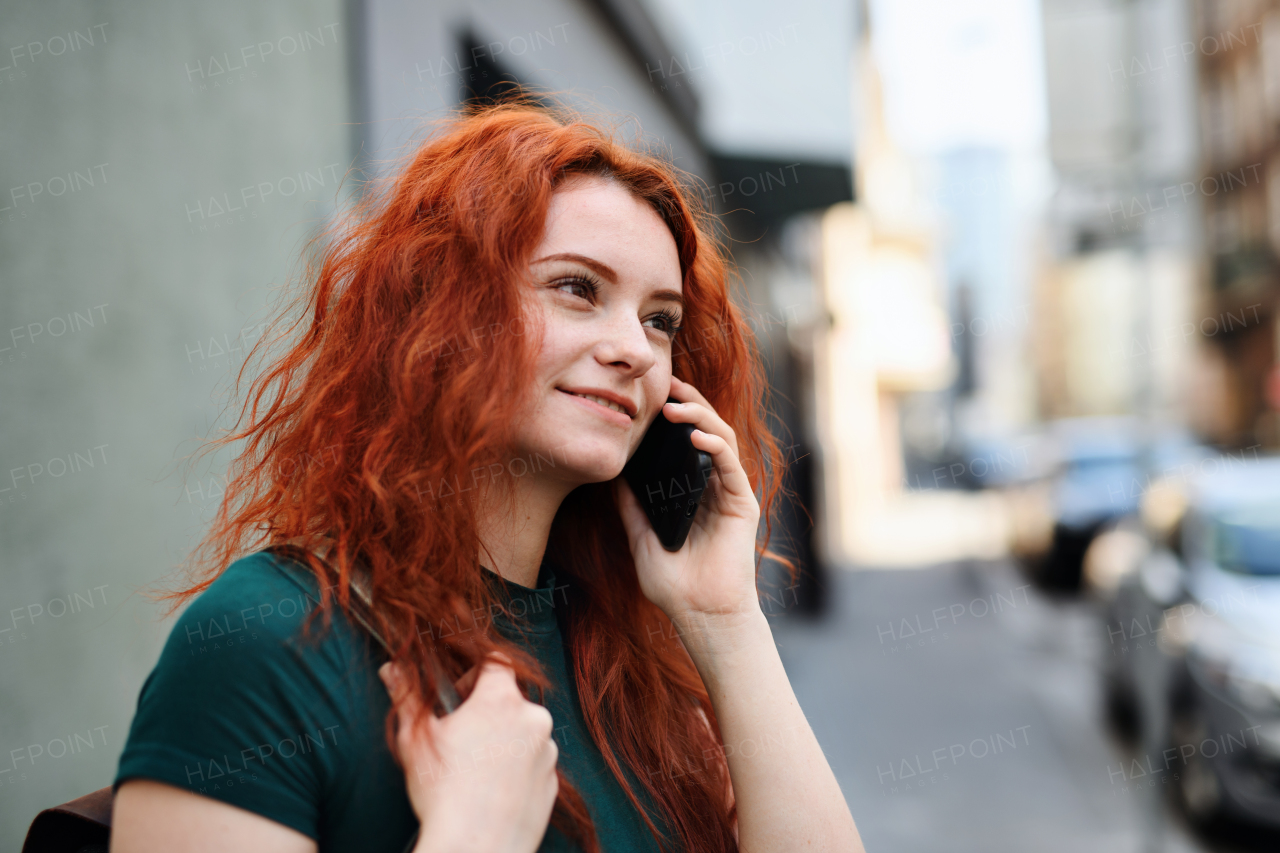 A portrait of young woman with backpack standing outdoors on city street, using smartphone.