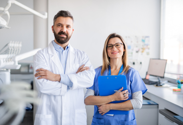 Front view of dentist with dental assistant in modern dental surgery, looking at camera.