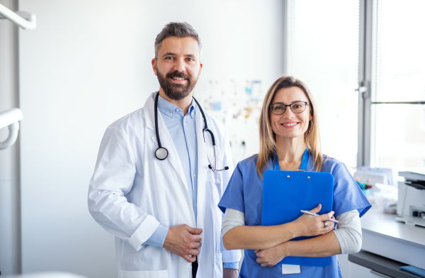 A front view portrait of dental assistant and dentist in modern dental surgery, looking at camera.