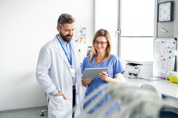 A front view portrait of dental assistant and dentist in modern dental surgery, using tablet.