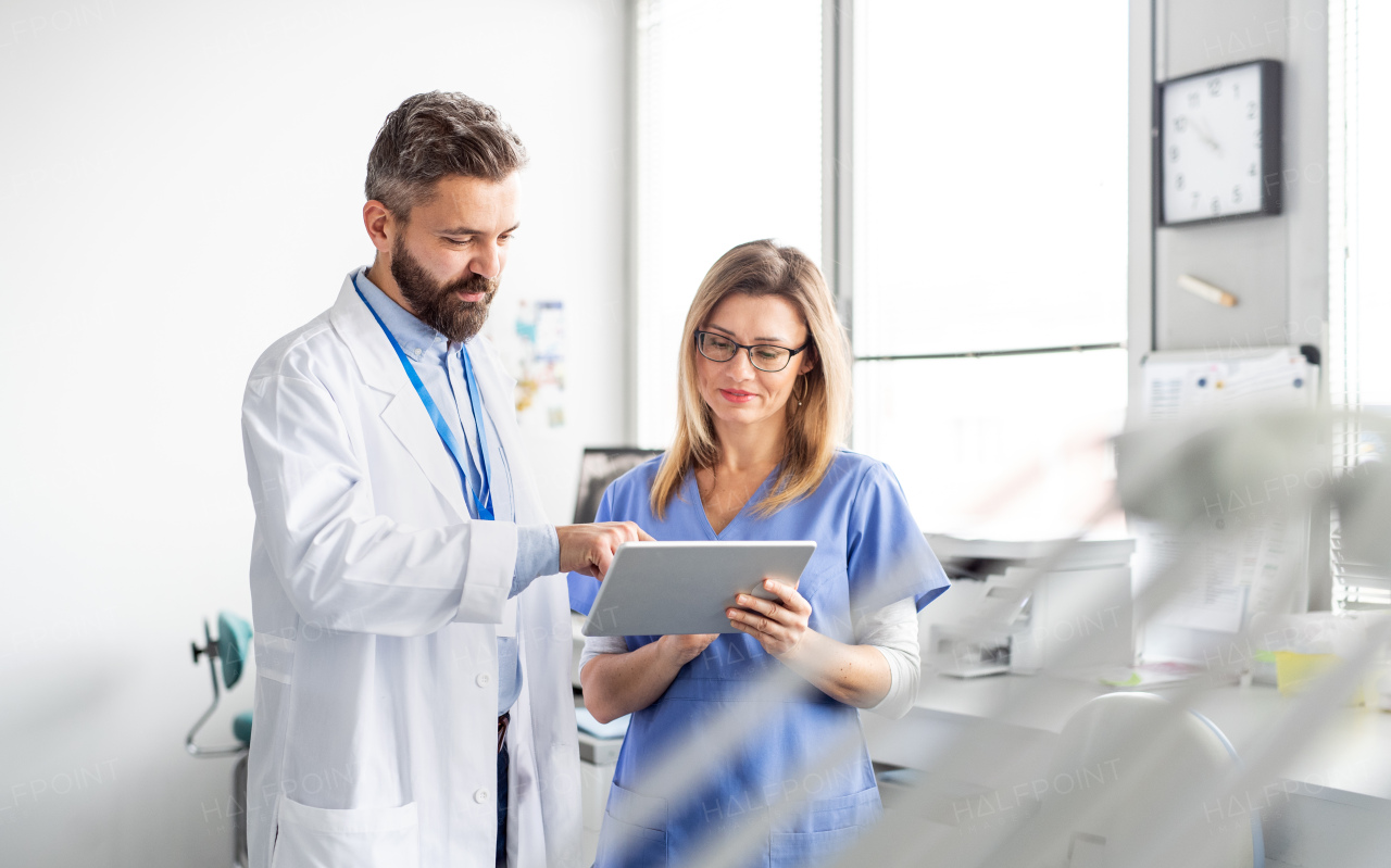 A front view portrait of dental assistant and dentist in modern dental surgery, using tablet.