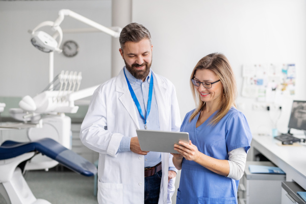 A front view portrait of dental assistant and dentist in modern dental surgery, using tablet.