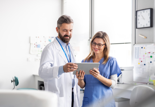 A front view portrait of dental assistant and dentist in modern dental surgery, using tablet.