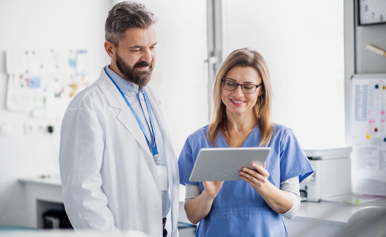 A front view portrait of dental assistant and dentist in modern dental surgery, using tablet.