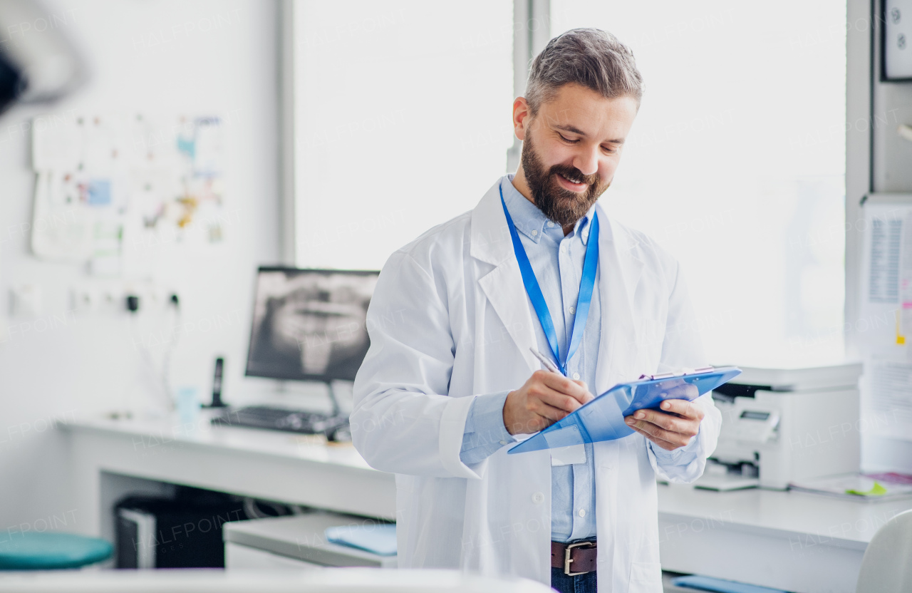 Mature dentist with clipboard in modern dental surgery, writing.