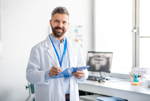 A mature dentist in modern dental surgery, loooking at camera.