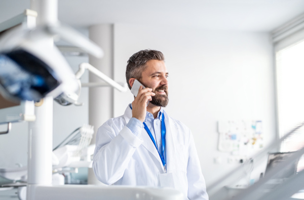 A mature dentist in modern dental surgery, using smartphone.