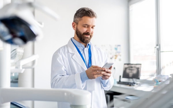 Mature dentist in modern dental surgery, using smartphone.