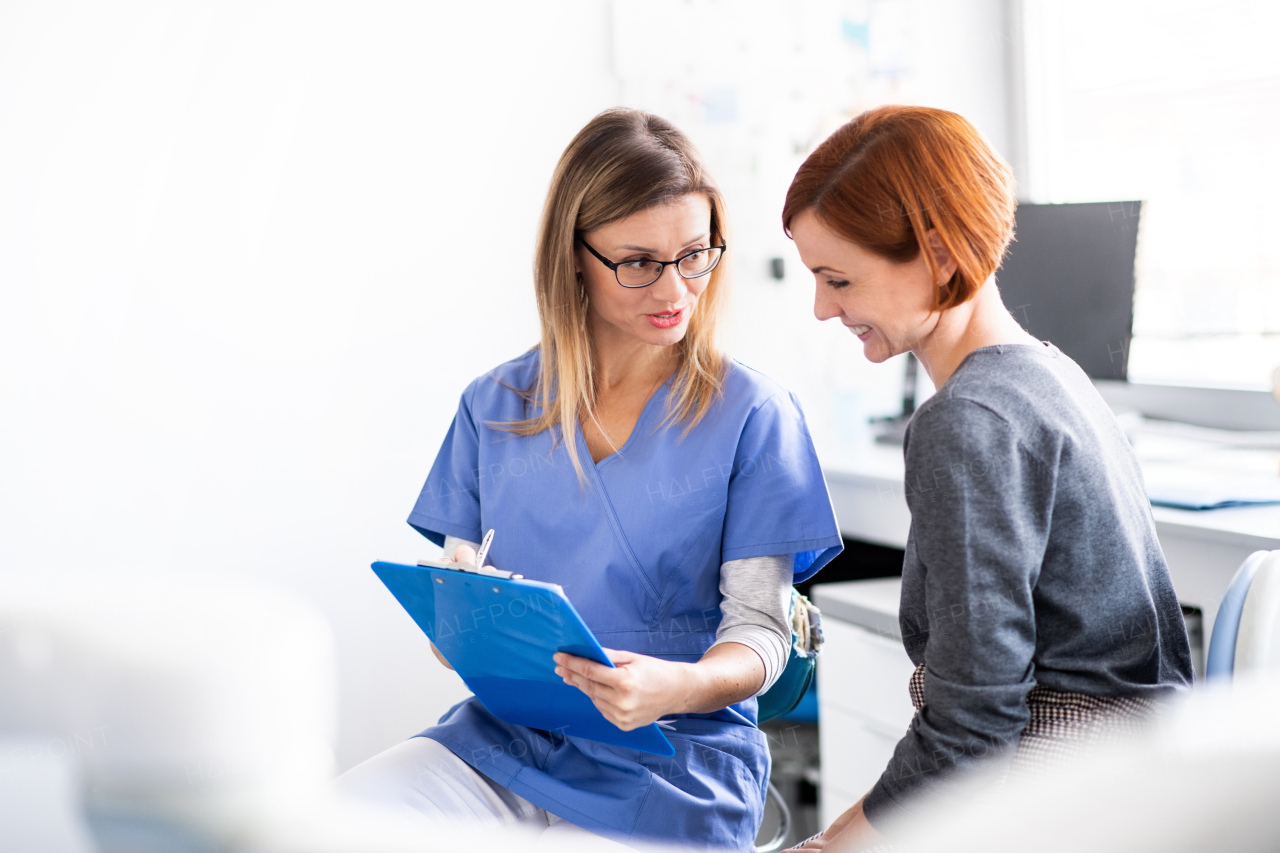 A dentist with clipboard talking to woman in dentist surgery, a dental check-up.