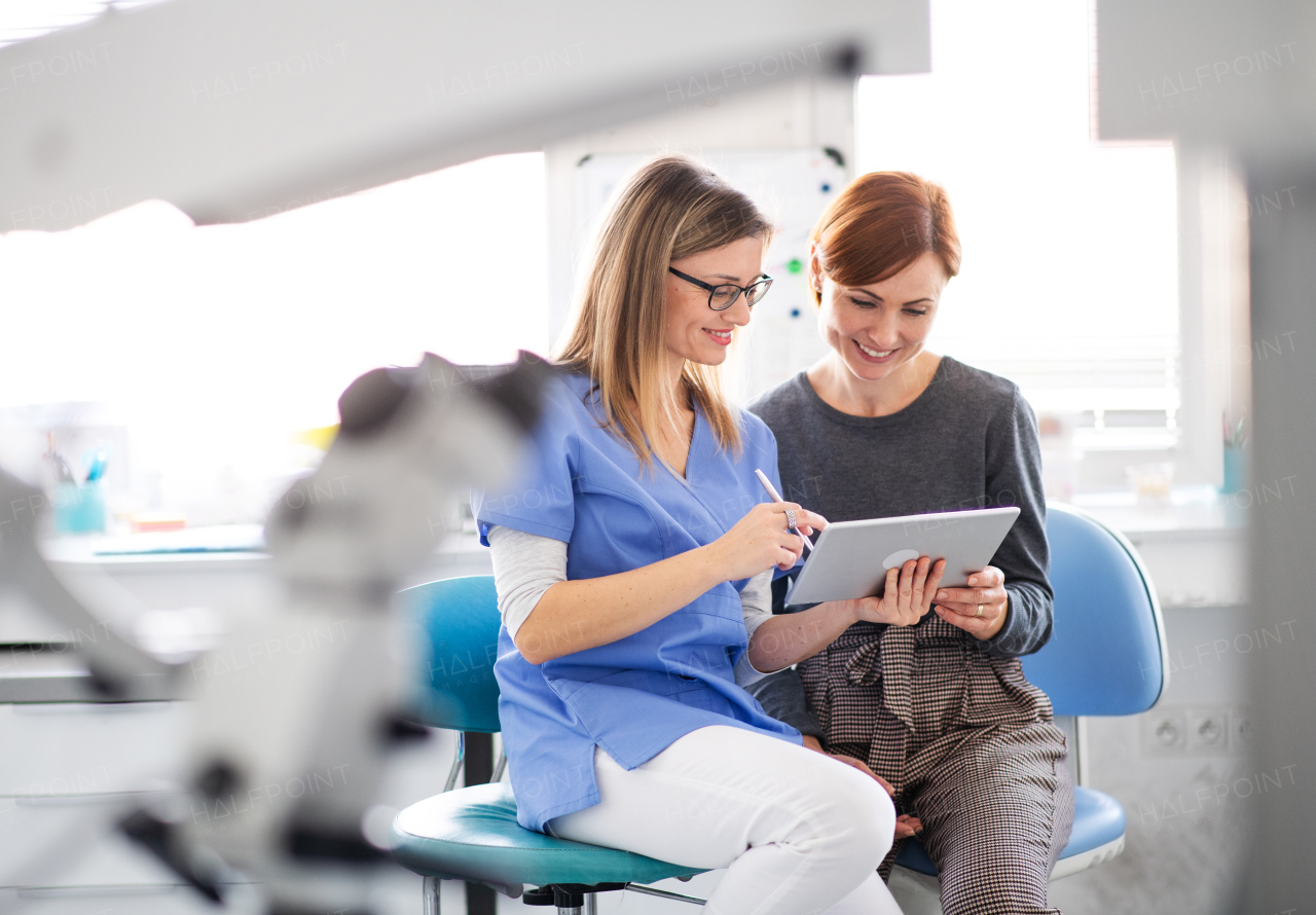 A dentist with tablet talking to woman in dentist surgery, a dental check-up.