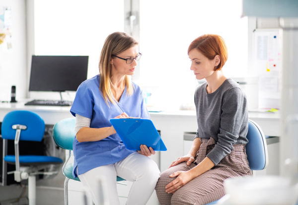 A dentist with clipboard talking to woman in dentist surgery, a dental check-up.