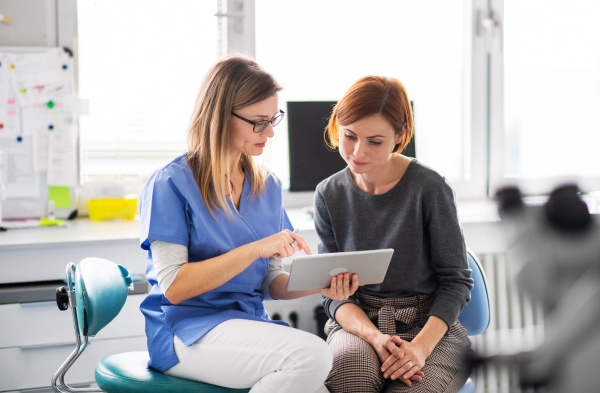 A dentist with tablet talking to woman in dentist surgery, a dental check-up.