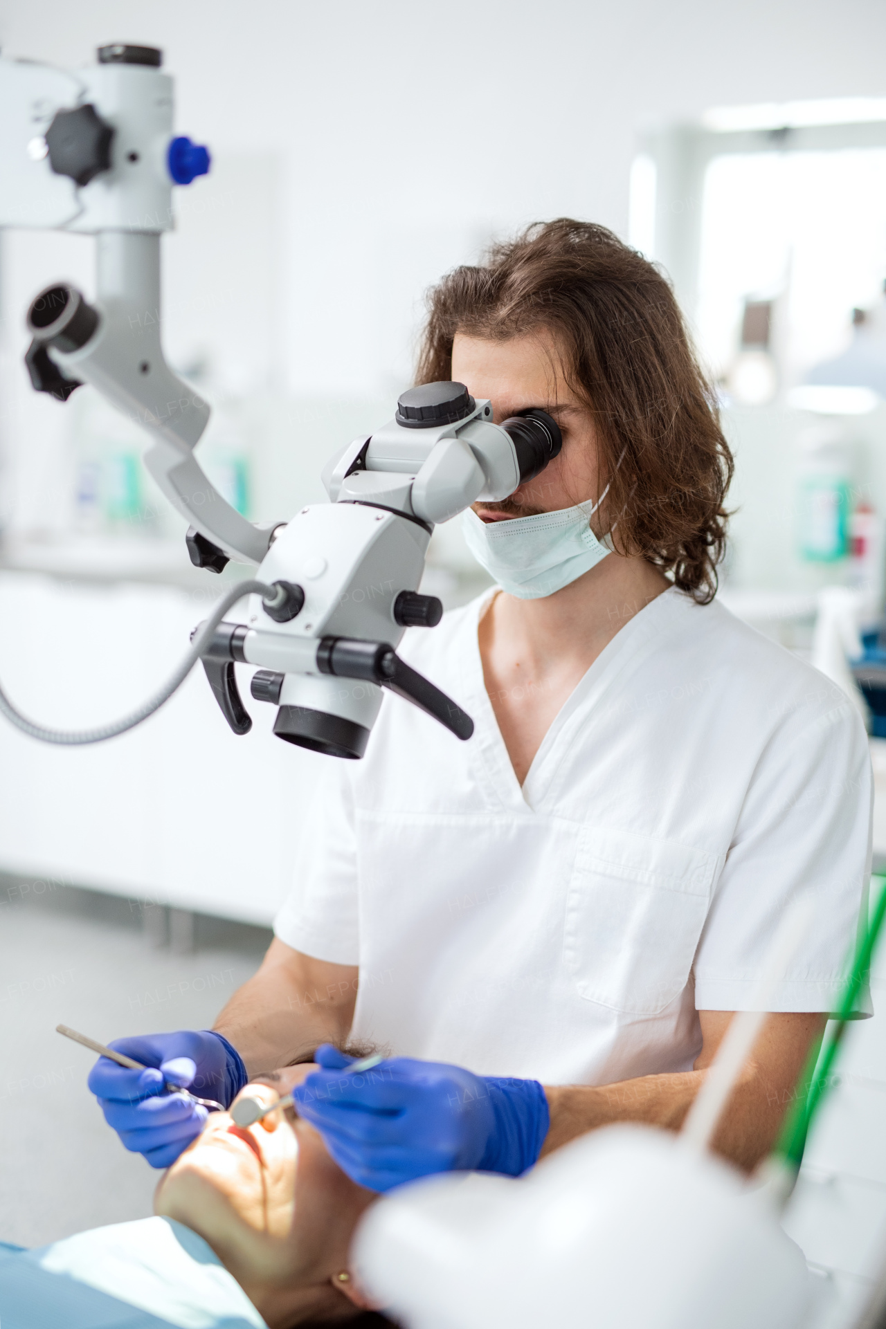 Man dentist with face mask and patient working in dental surgery.