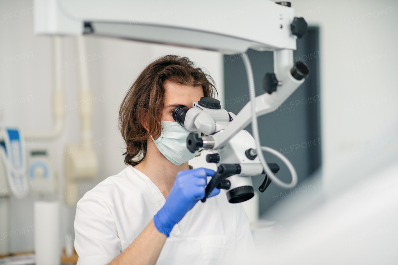 Unrecognizable young dentist with face mask working in dental surgery.