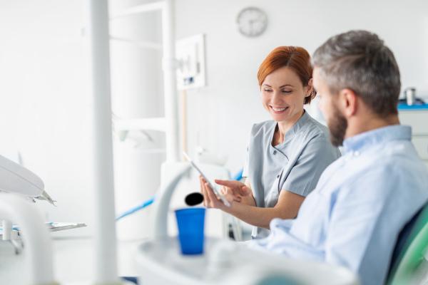 Side view of dentist with tablet talking to man in dentist surgery, a dental check-up.