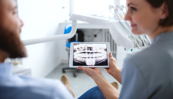 Rear view of dentist with tablet talking to man in dentist surgery, a dental check-up.