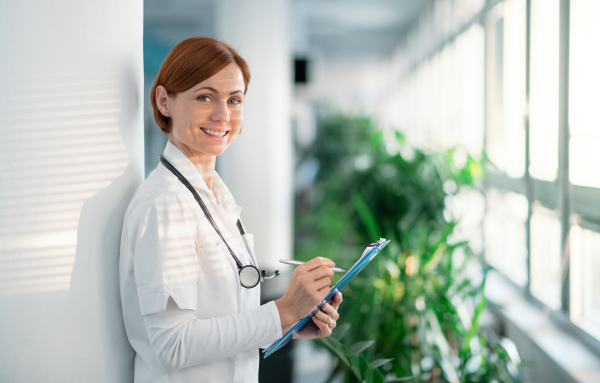 Portrait of woman doctor with clipboard standing in hospital. Copy space.