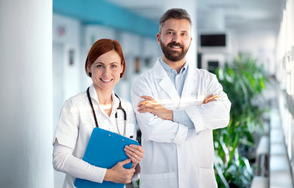 A portrait of man and woman doctor standing in hospital, looking at camera.