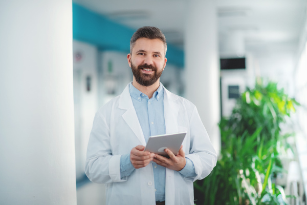 Portrait of man doctor standing in hospital, using tablet. Copy space.