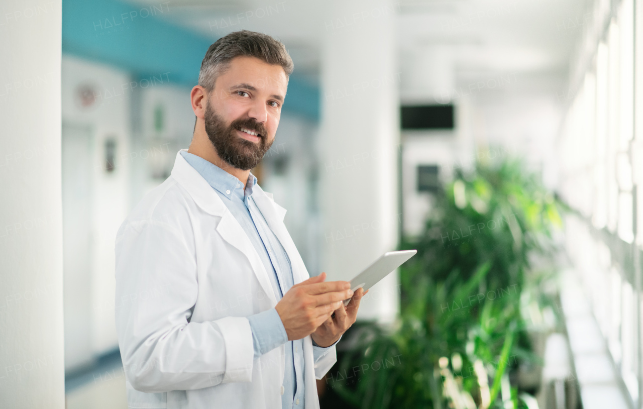 Portrait of man doctor standing in hospital, using tablet. Copy space.