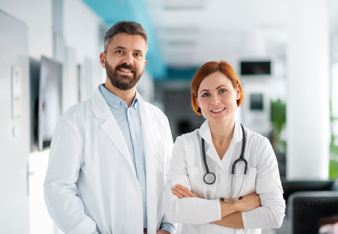 A portrait of man and woman doctor standing in hospital, looking at camera.