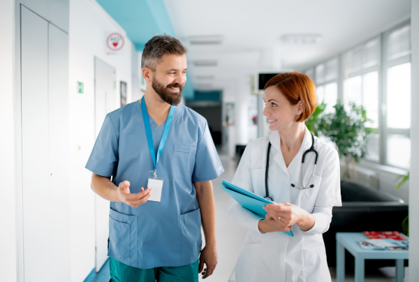 A portrait of man and woman doctor walking in hospital, talking.