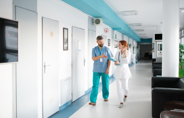 Portrait of man and woman doctor walking in hospital, talking. Copy space.